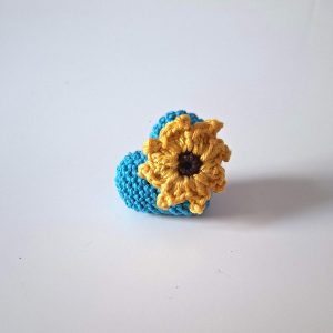 Acest accesoriu îmbină simbolul iubirii – o inimă croșetată într-un albastru vibrant – cu optimismul și lumina florii-soarelui, aplicată manual petală cu petală. Cum o poți purta? Prinde-o pe haină, pe eșarfă sau pe geanta preferată pentru a adăuga un strop de culoare și personalitate ținutei tale. Un cadou inedit pentru cineva drag sau un suvenir special care îți va aminti mereu de momentele însorite!